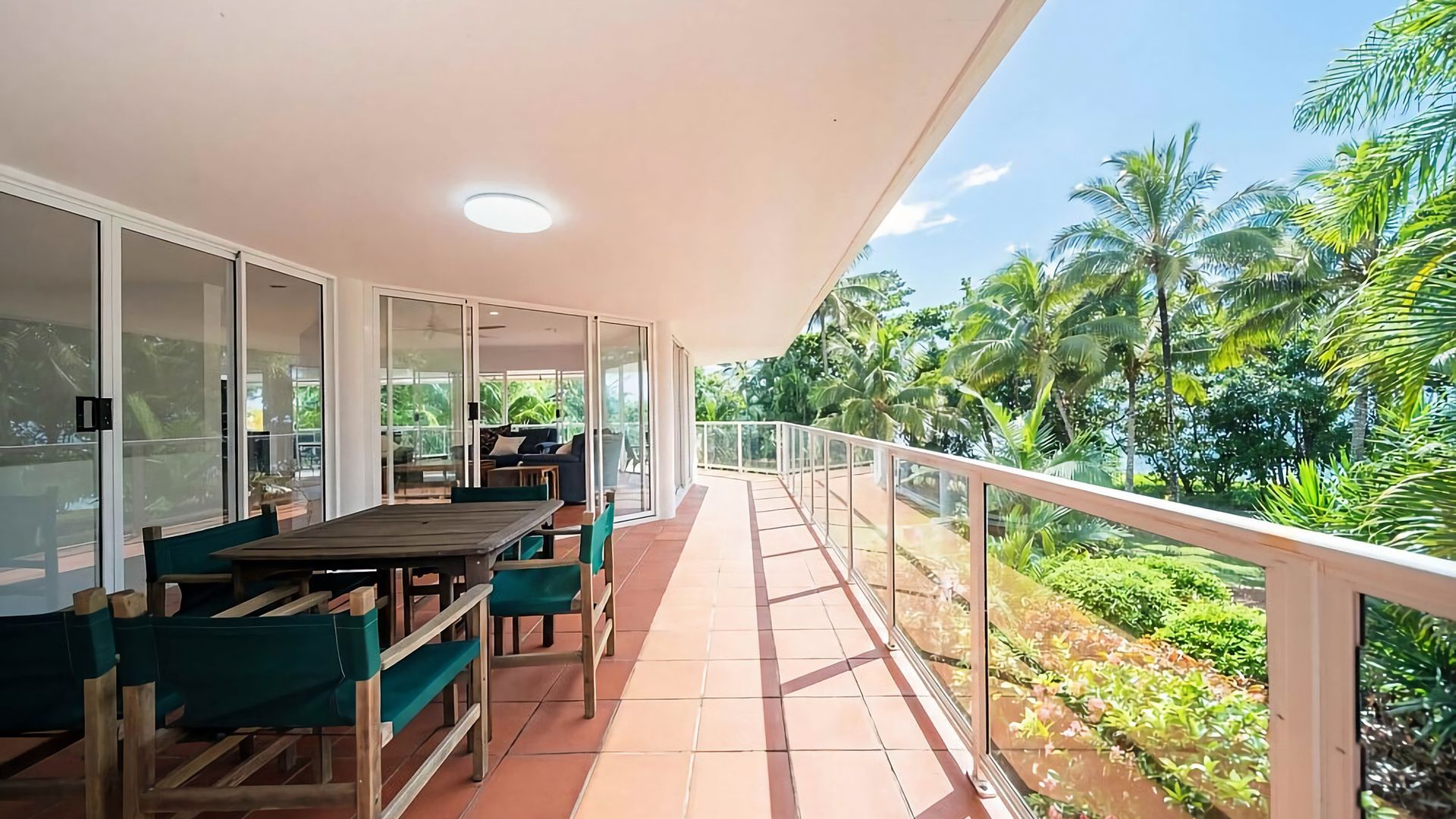 A balcony with a wooden table and chairs, a sofa, and a glass door leading to an indoor area.