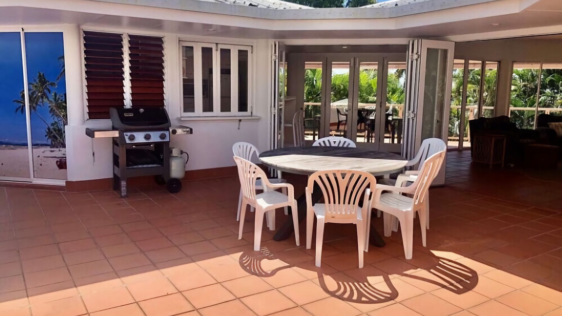 Un patio al aire libre con una mesa redonda y sillas, una parrilla y vista a la playa a través de puertas corredizas de vidrio.