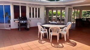 An outdoor patio area with a round table and chairs, a grill, and a view of the beach through the sliding glass doors. - Beaches No 6 - Beachfront Views (Wongaling Beach)