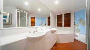 A modern bathroom with a large mirror, two sinks, and a bathtub.
