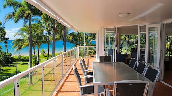 A balcony with a glass railing overlooking a beach with palm trees and the ocean.