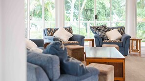 A modern living room with two sofas, a coffee table, and a view of greenery through large windows.