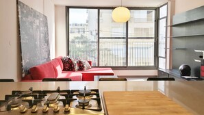 Une cuisine moderne avec une cuisinière à gaz, une table en bois et un canapé rouge près d’une grande fenêtre.