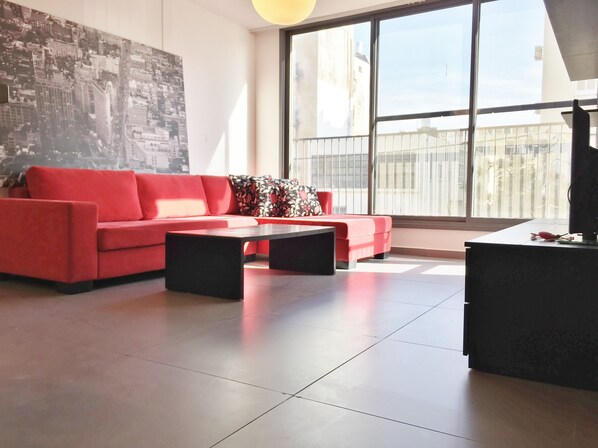 A modern living room with a red sofa, a black coffee table, and a large window with a view of buildings.