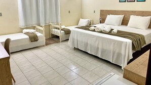 A hotel room with two single beds, a double bed, a wooden headboard, a small table, a chair, a bathroom with a shower curtain, and three framed pictures on the wall. - Country house, heated pool, beach, tennis court, barbecue, playground, fishing, pets allowed. (Barão de Antonina)