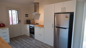 Una cocina con gabinetes blancos, un refrigerador de acero inoxidable, un microondas, un horno y una estufa a gas.