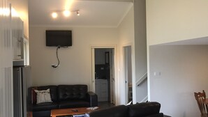 Una sala de estar con un sofá de cuero negro, una mesa de centro de madera y un televisor de pantalla plana montado en la pared.