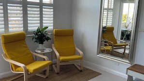 A room with two yellow armchairs, a small round table, a large mirror, and a view of the outdoors through a window with blinds. - bondi beach  studio 8  balcony  rooftop pool, aircon, walk to beach, restaurants (Bondi Beach)