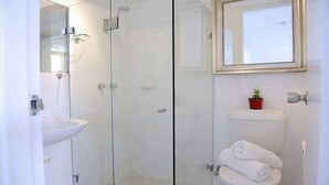 Une salle de bain moderne avec une douche à parois de verre, un lavabo blanc et des toilettes dotées d’un porte-serviettes.