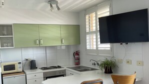 A modern kitchen with white cabinets, a microwave, a kettle, and a small refrigerator. There is a bar counter with two stools and a flat-screen TV mounted above it. - bondi beach  studio 8  balcony  rooftop pool, aircon, walk to beach, restaurants (Bondi Beach)