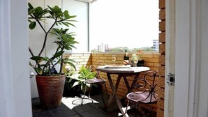 Une petite terrasse extérieure avec une table et des chaises, un pot de fleurs et une vue sur le paysage urbain.