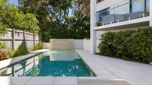 A modern pool area with a stone wall, surrounded by a wooden fence and lush greenery.