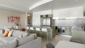 A modern kitchen with a central island, stainless steel appliances, and a dining area with white chairs.