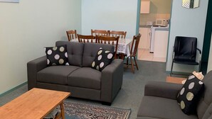 A living room with a sofa, two armchairs, a wooden coffee table, and a dining area with a table and chairs.