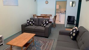 A living room with two sofas, a wooden coffee table, a patterned rug, and a dining area with a table and chairs.