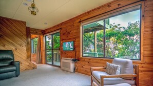 Una habitación acogedora con paredes de madera, ventanas amplias, un sofá de cuero negro, una silla de madera y una televisión.