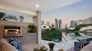 A modern outdoor kitchen with a city skyline view, a dining area with a table and chairs, and a poolside setting.