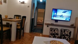 Una sala de estar con comedor, un televisor montado en la pared y un sofá con cojines estampados.