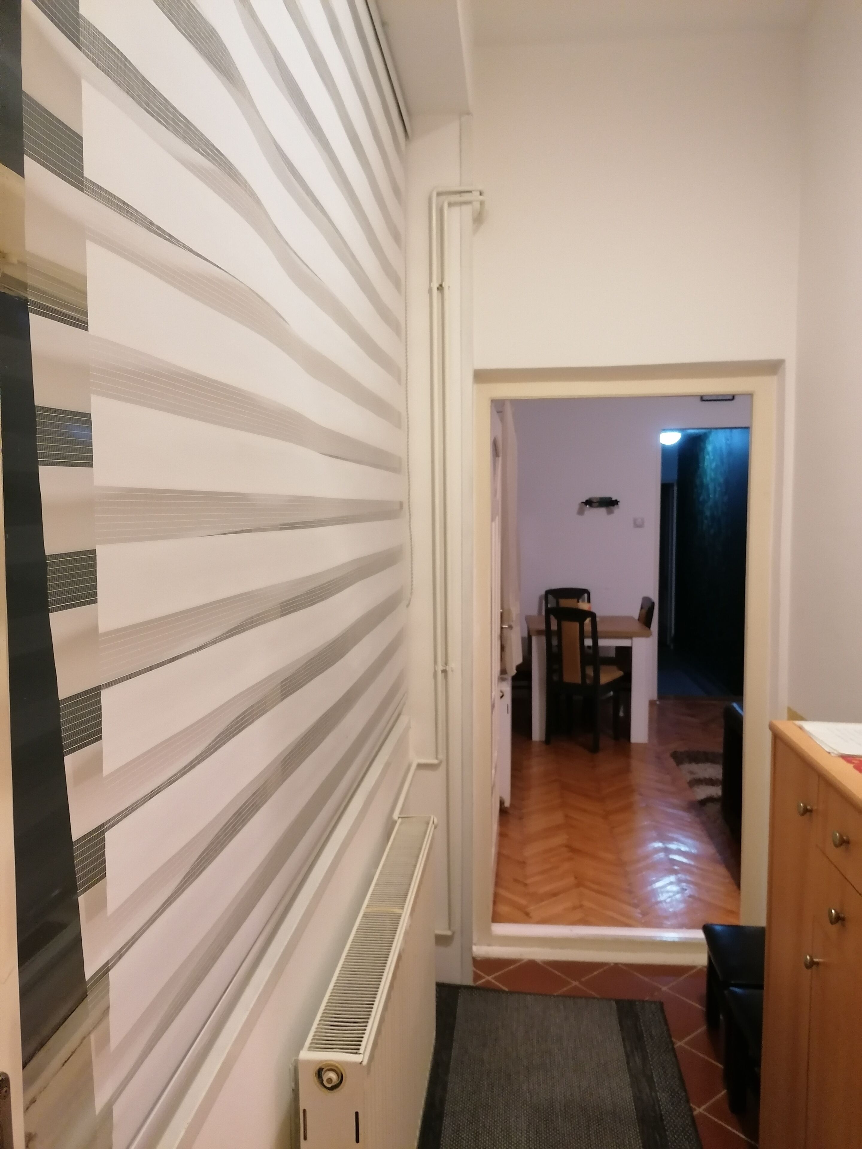 A hallway with striped wallpaper, a radiator, a wooden floor, and a view into a dining area with a table and chairs.