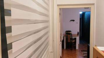 A hallway with striped wallpaper, a radiator, a wooden floor, and a view into a dining area with a table and chairs.