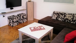 Una sala de estar con un televisor de pantalla plana, un sofá, una mesa de centro y otomanas estampadas.