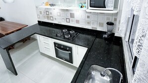 Una cocina moderna con armarios blancos, encimera negra, pileta de acero inoxidable, microondas y estufa a gas.