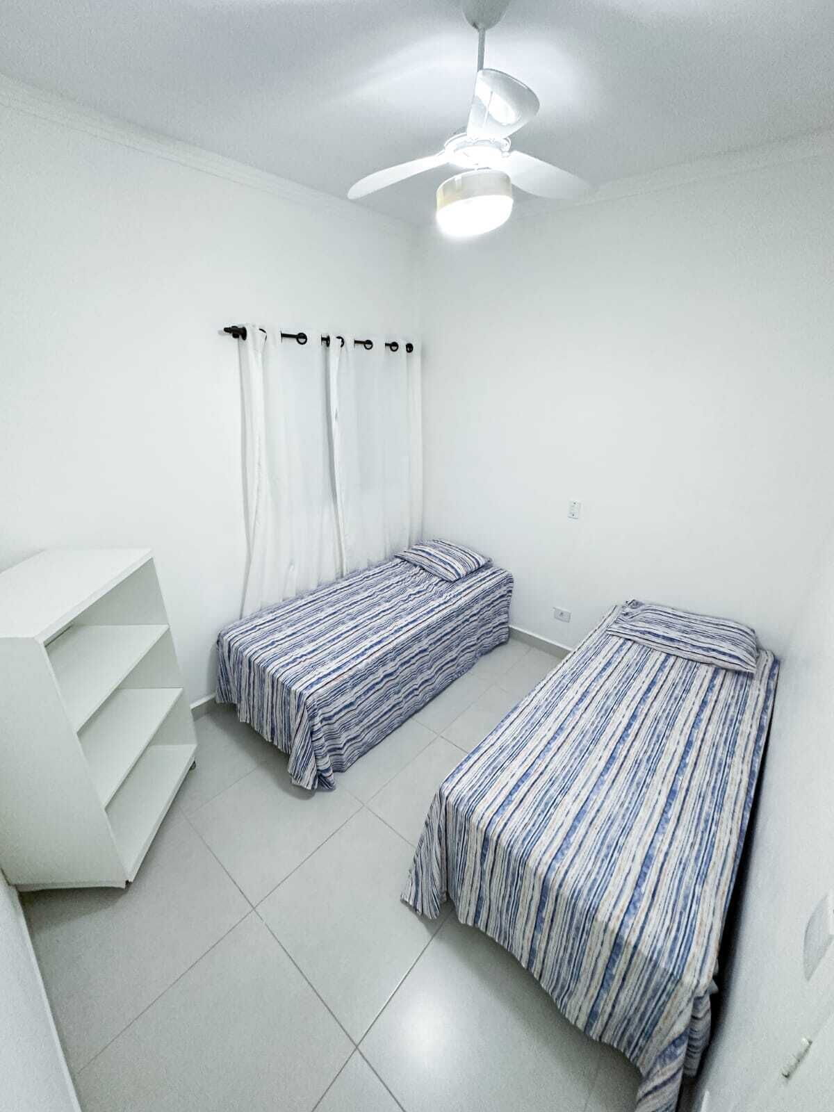 A room with two beds, a ceiling fan, and a white shelving unit.