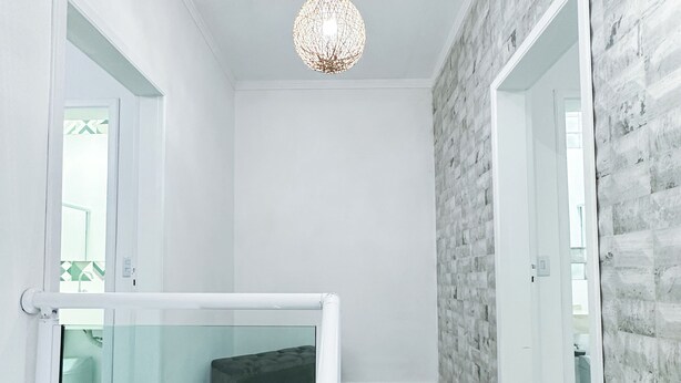 Un interior moderno con una escalera, una lámpara colgante y vista a otra habitación.