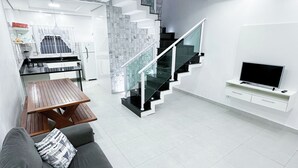 Una sala de estar moderna con un sofá gris, una mesa de madera, una escalera y un televisor montado en la pared.