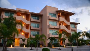 Un hôtel à plusieurs étages doté de balcons, de palmiers et d’un éclairage extérieur.