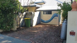 Una zona residencial con un camino pavimentado que conduce a una casa con techo de tejas y un muro de mosaico que representa una ola y la palabra 'SEA'.