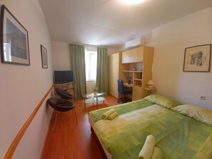 A hotel room with a bed, a desk, a chair, a television, and a wardrobe.