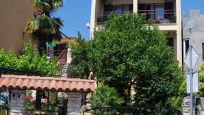 Un bâtiment à deux étages doté d’un balcon, d’un mur en pierre et d’un arbre devant.