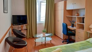Une petite chambre comprenant un lit, un bureau, une chaise, un téléviseur et une armoire.