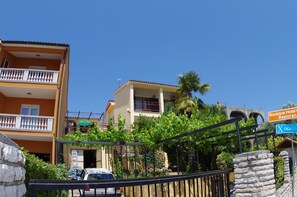 A two-story building with a balcony, a car parked in front, and a stone wall.