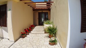 Une cour étroite avec un sol carrelé, des plantes en pot et une pergola en bois.