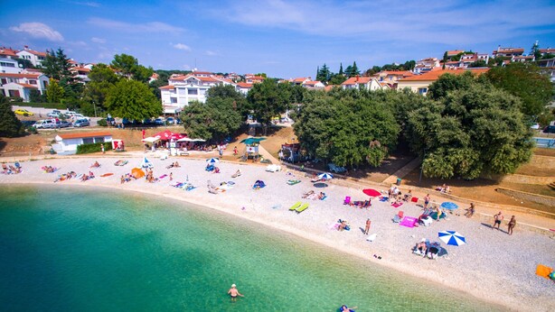 Une plage avec une eau turquoise et limpide, des parasols et des gens qui prennent des bains de soleil.