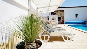 A poolside area with lounge chairs, a potted plant, and a brick oven.