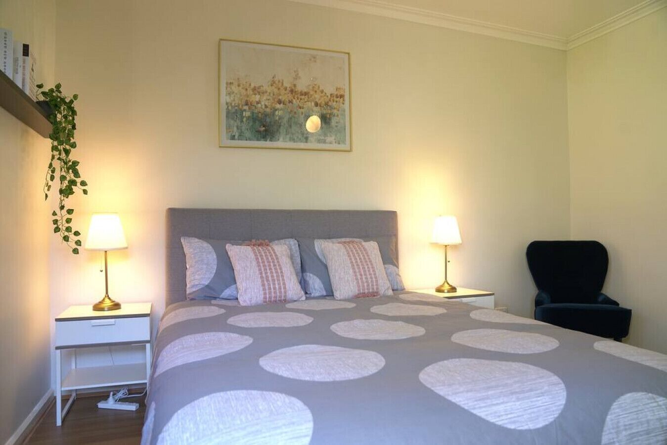 Quarto bem organizado com uma cama grande, duas mesas de cabeceira, uma cadeira e um quadro pendurado na parede.