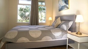 A bedroom with a large bed, two bedside lamps, a window with curtains, and a painting on the wall.