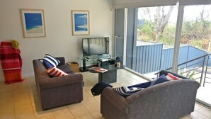 Una sala de estar con dos sofás, un televisor y una mesa de centro de vidrio. Hay dos cuadros en la pared y una manta roja en el suelo.