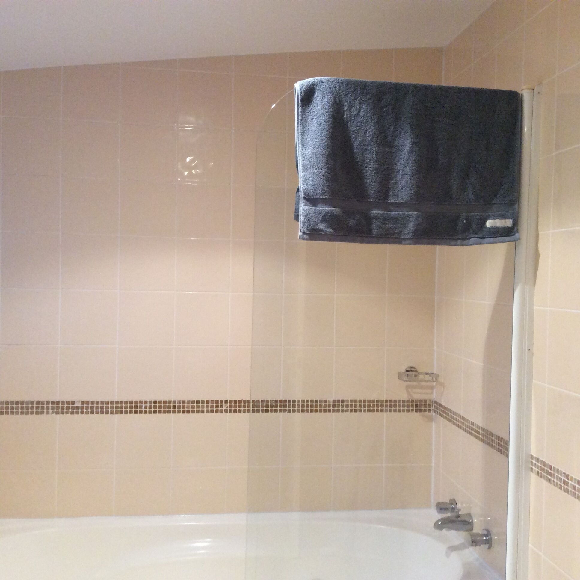 Un bagno con una vasca, un asciugamano su un portasci e una parete piastrellata con decorazione.