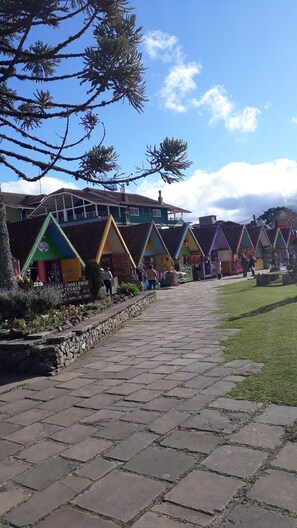 A pathway leading to colorful, triangular-roofed buildings with stone walls and a stone bench. - Duplex apartment. One block from the Stone Cathedral. (Canela)