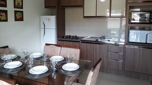 A modern kitchen with wooden cabinets, a built-in oven, and a dining area set for four with a glass table and chairs. - Duplex apartment. One block from the Stone Cathedral. (Canela)
