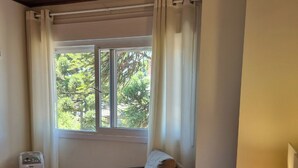 A bedroom with a bed, a chair, a bedside table with a lamp, a window with curtains, and a radiator. - Duplex apartment. One block from the Stone Cathedral. (Canela)