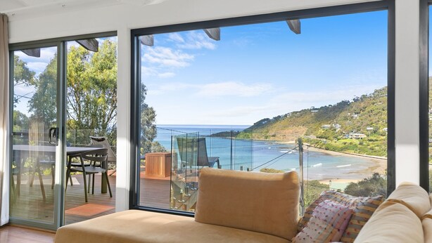 Een moderne woonkamer met een grote schuifglazen deur die uitkomt op een balkon met uitzicht op de oceaan en heuvels.