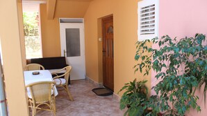 Ein kleiner Patio-Bereich mit Korbmöbeln, einer weißen Tür und Topfpflanzen.