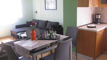 Un comedor con una mesa lista para dos personas, un sofá y una zona de cocina con cafetera.