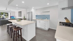 Una cocina moderna con una isla central, taburetes de bar, horno empotrado y un ventanal amplio.