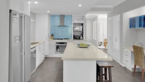 Una cocina moderna con armarios blancos, una isla central y una campana extractora azul.